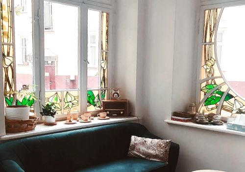 Na zdjęciu widać fragment werandy, stanowiącej część poczekalni w Ośrodku Promocji Zdrowia i Terapii Uzależnień. Na zdjęciu uchwycono okna z pięknymi witrażami oraz fragment pluszowej kanapy.okna z